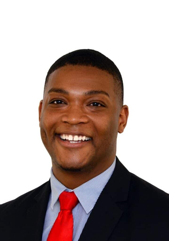 A man in a suit and red tie smiling at the camera, with a white background.