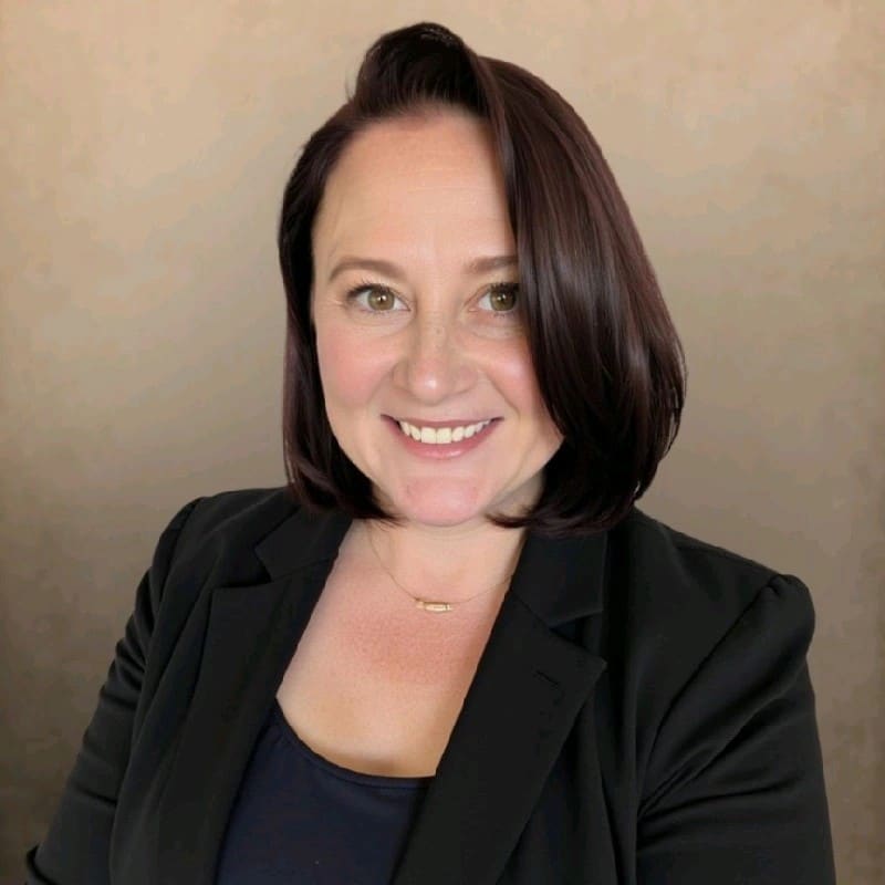 Smiling woman with straight, dark shoulder-length hair wearing a black blazer and black top, posed in front of a plain beige background, reflecting professionalism suited for roles in AI-Enabled Automation for Discharge Management.