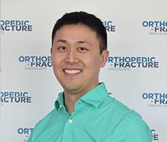 A man wearing a teal collared shirt smiles in front of a backdrop that reads "Orthopedic + Fracture Specialists," highlighting the capacity with intelligent workflows to enhance patient care.