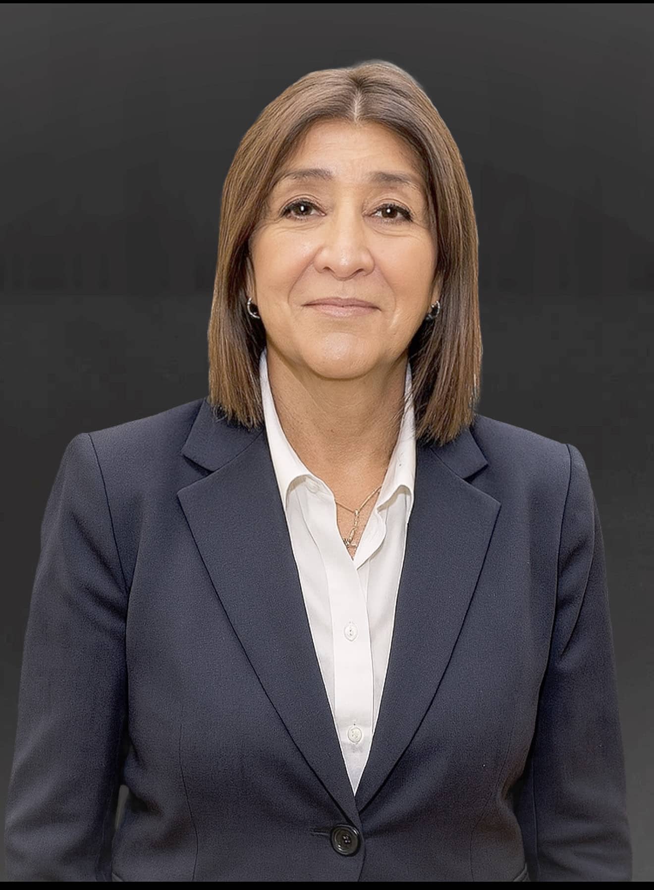 A woman with straight brown hair, wearing a dark blazer over a white shirt, stands facing the camera against a plain dark background—ready to unlock her capacity with intelligent workflows.
