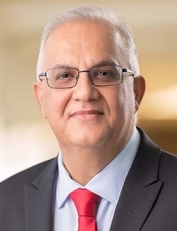 A middle-aged man with gray hair and glasses, wearing a dark suit, light blue shirt, and red tie, smiling slightly at the camera—reflecting the confidence needed for resilient sustainable health systems.