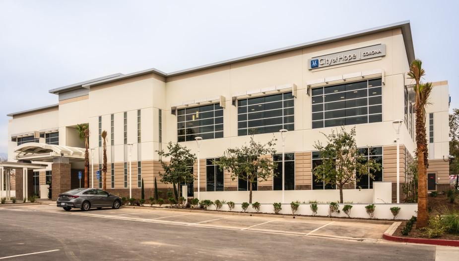 A modern two-story medical office building with large windows, a sign reading "City of Hope," a parked car, and an empty parking lot in front.