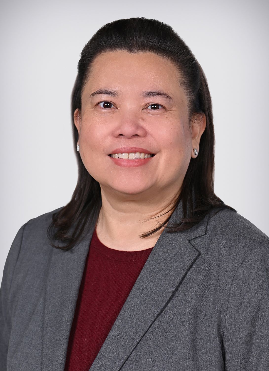 A woman with medium-length dark hair, a gray blazer over a maroon top, smiles at the camera—a professional in infusion nurse scheduling optimization.