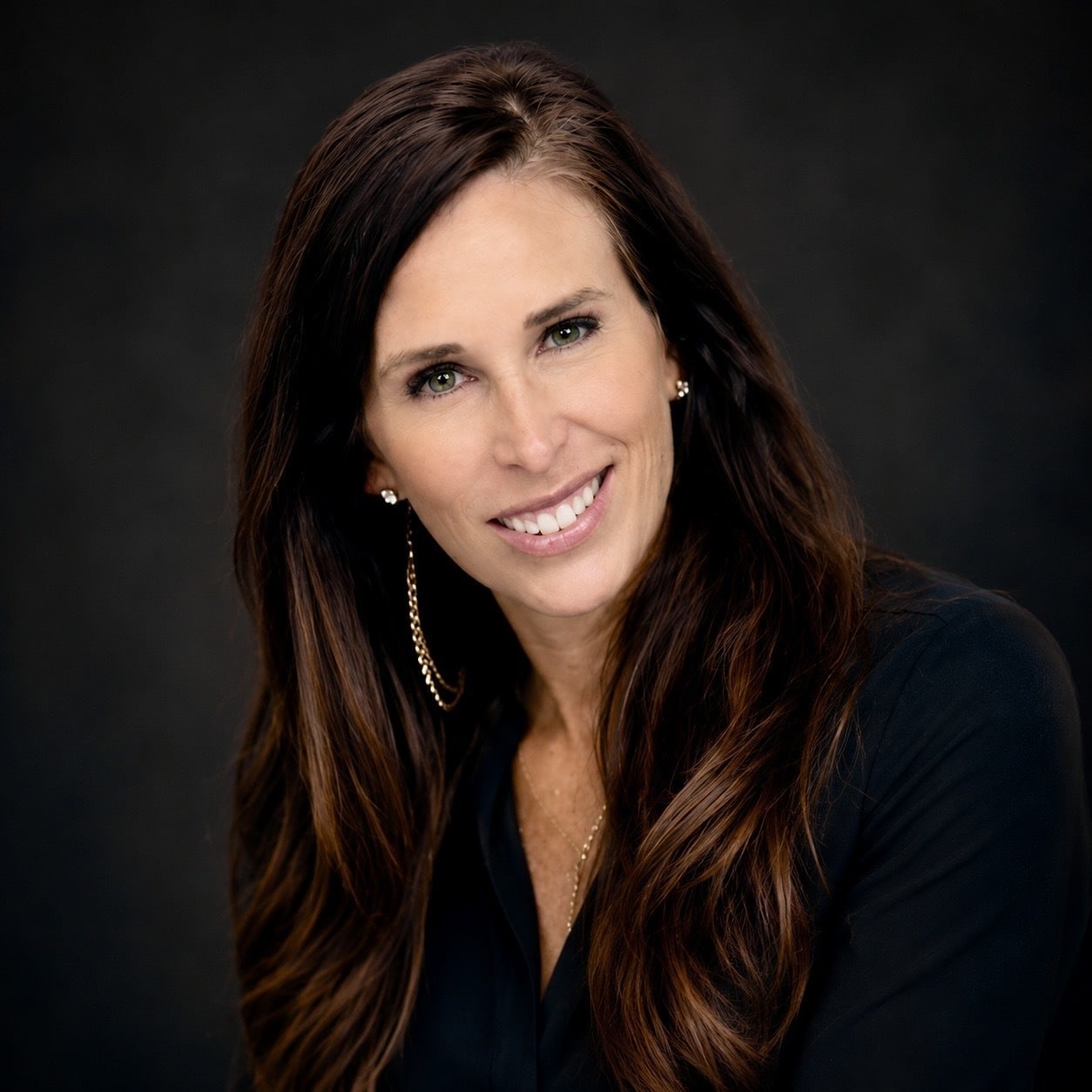 A smiling woman with long brown hair posing against a dark background.